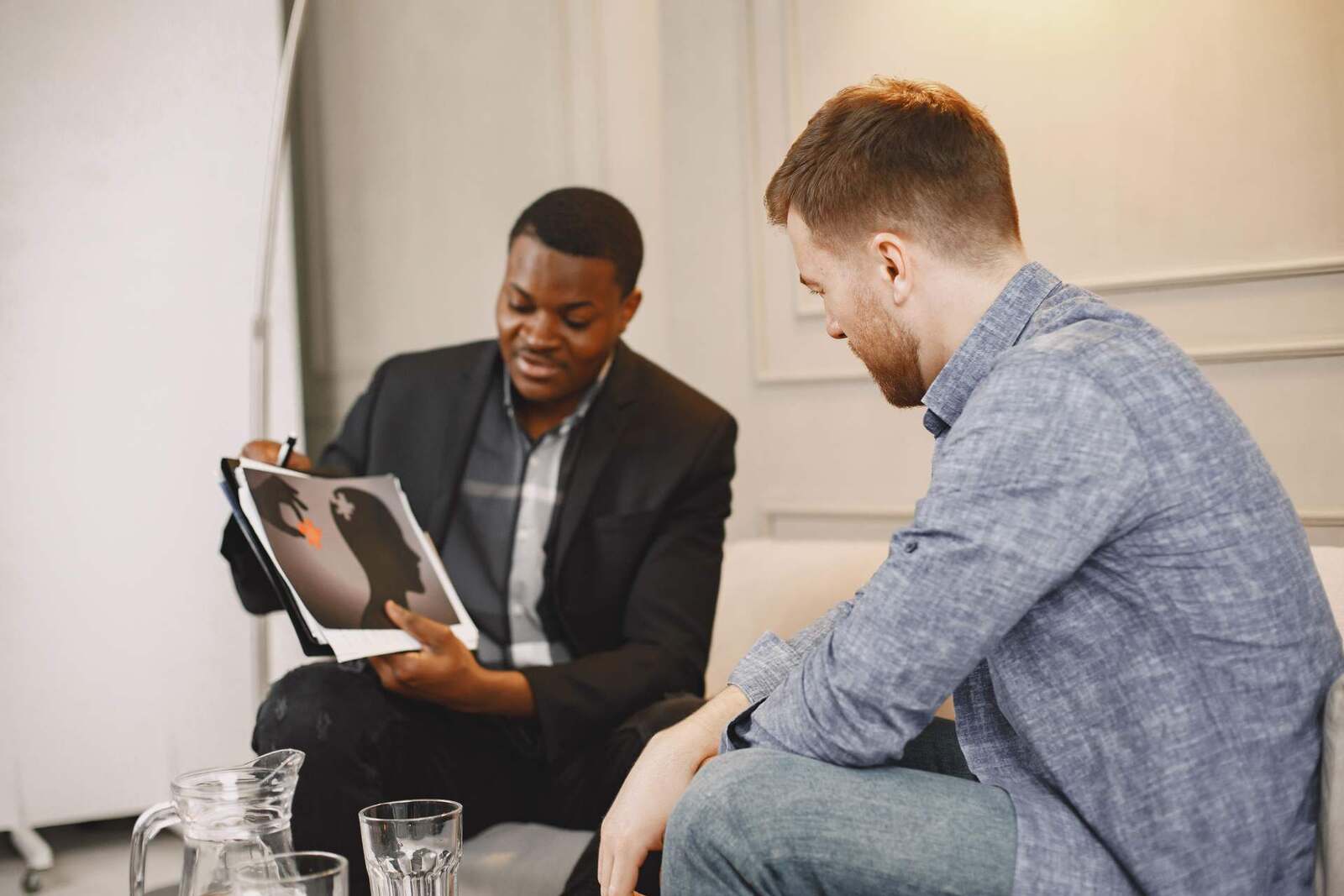 A counsellor shows a client an illustrated guide to mental health risks during a consultation in a bright room, standing in for the antidepressant safety review