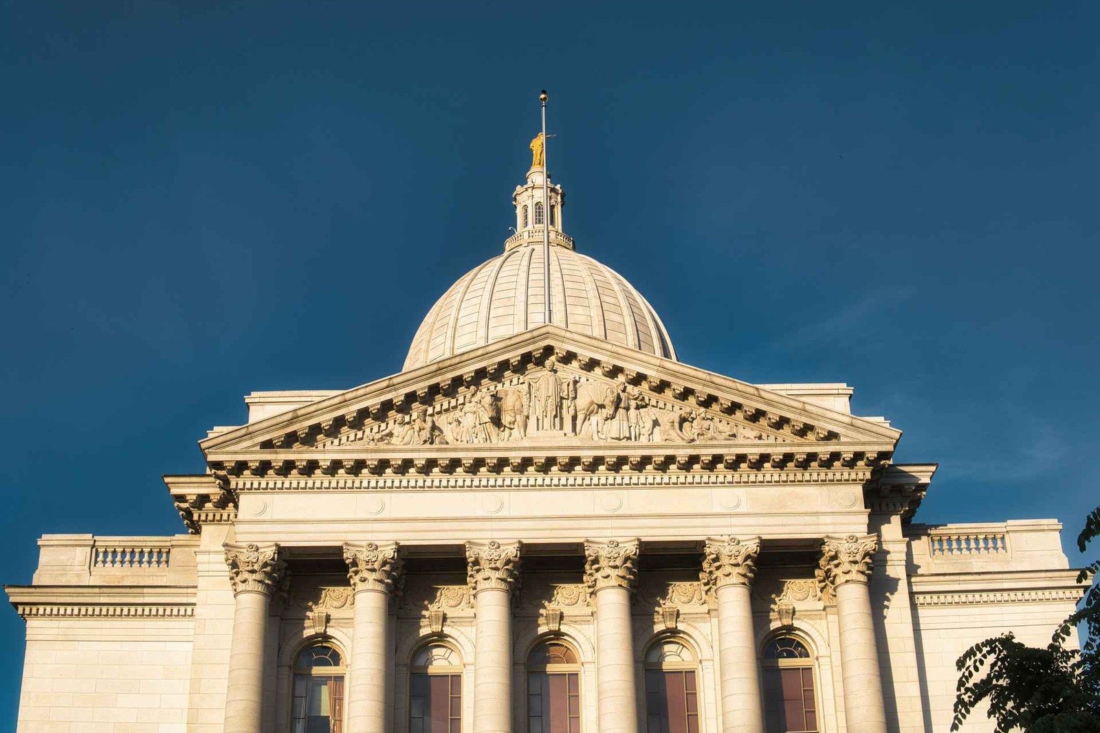 A low sun lights the dome and pediment of a neoclassical government capitol building against a deep blue sky