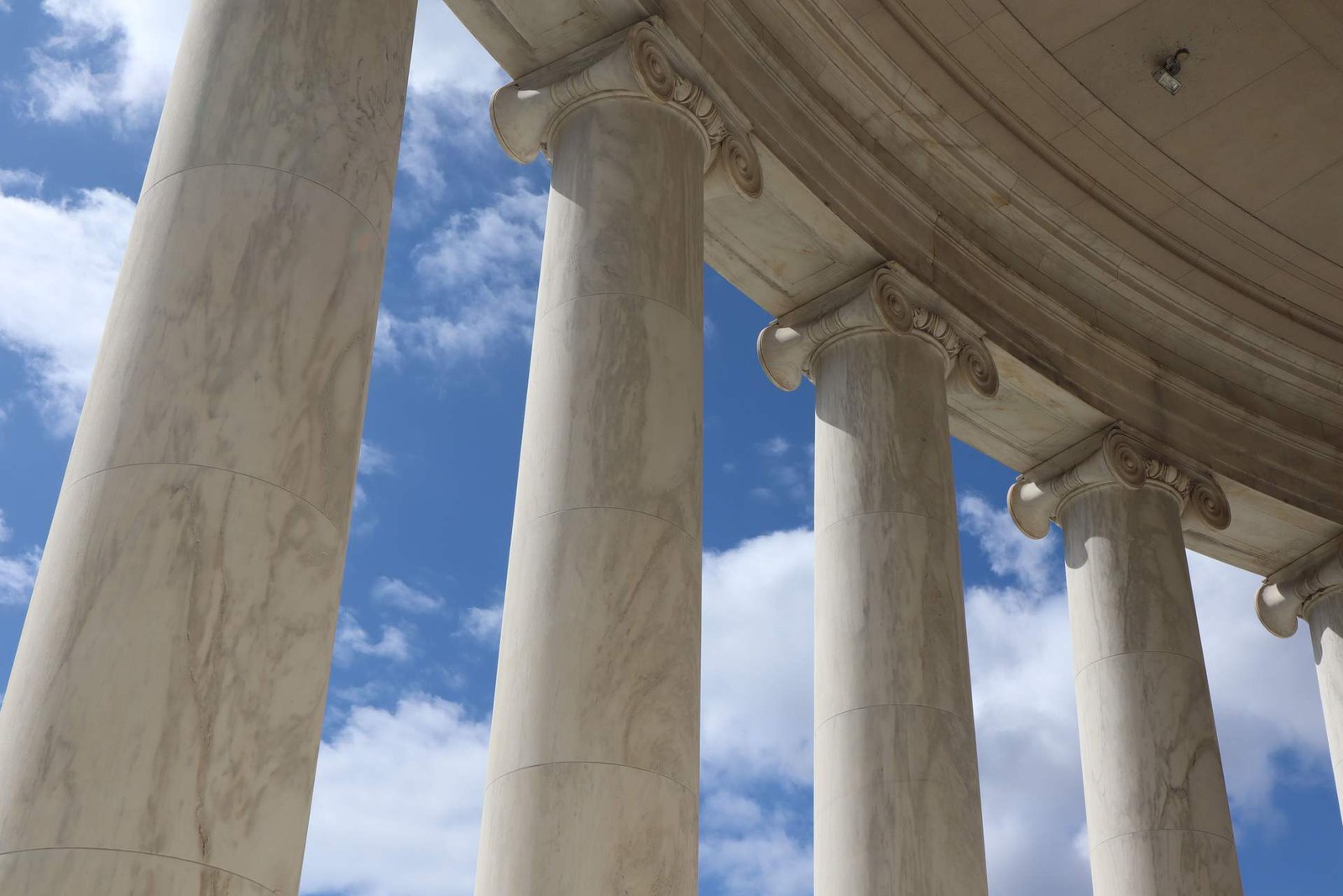 Marble columns and rotunda ceiling of a neoclassical government building, viewed from below against a blue sky