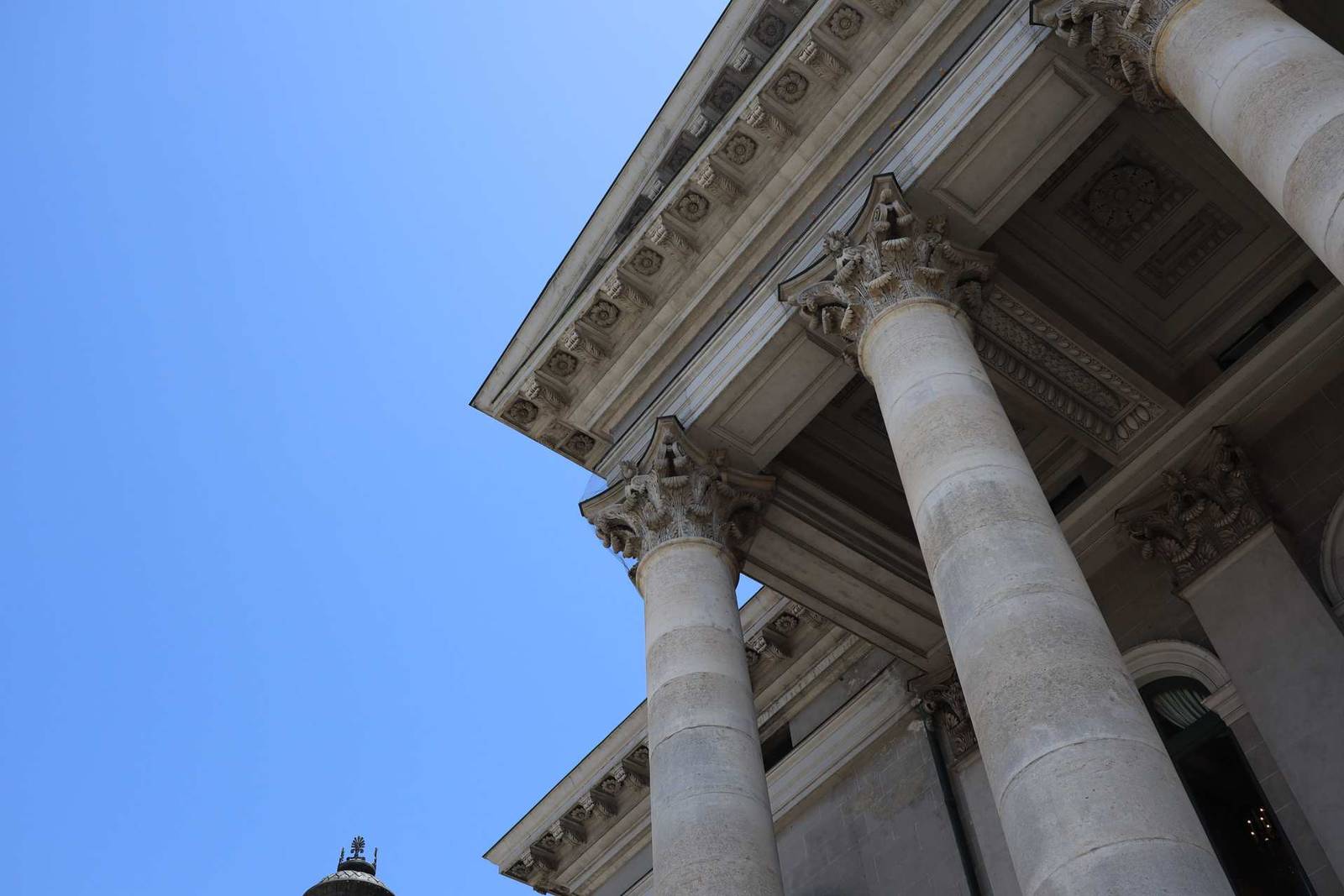 Looking up at the columns and carved pediment of a neoclassical courthouse against a clear blue sky