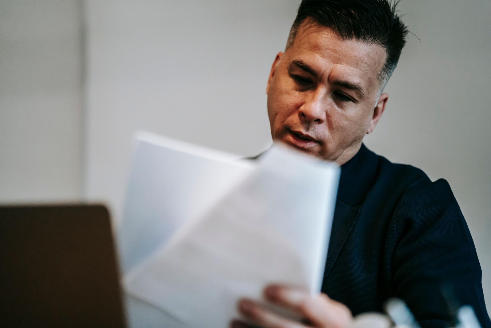 A man in a dark suit closely reads a folded paper document
