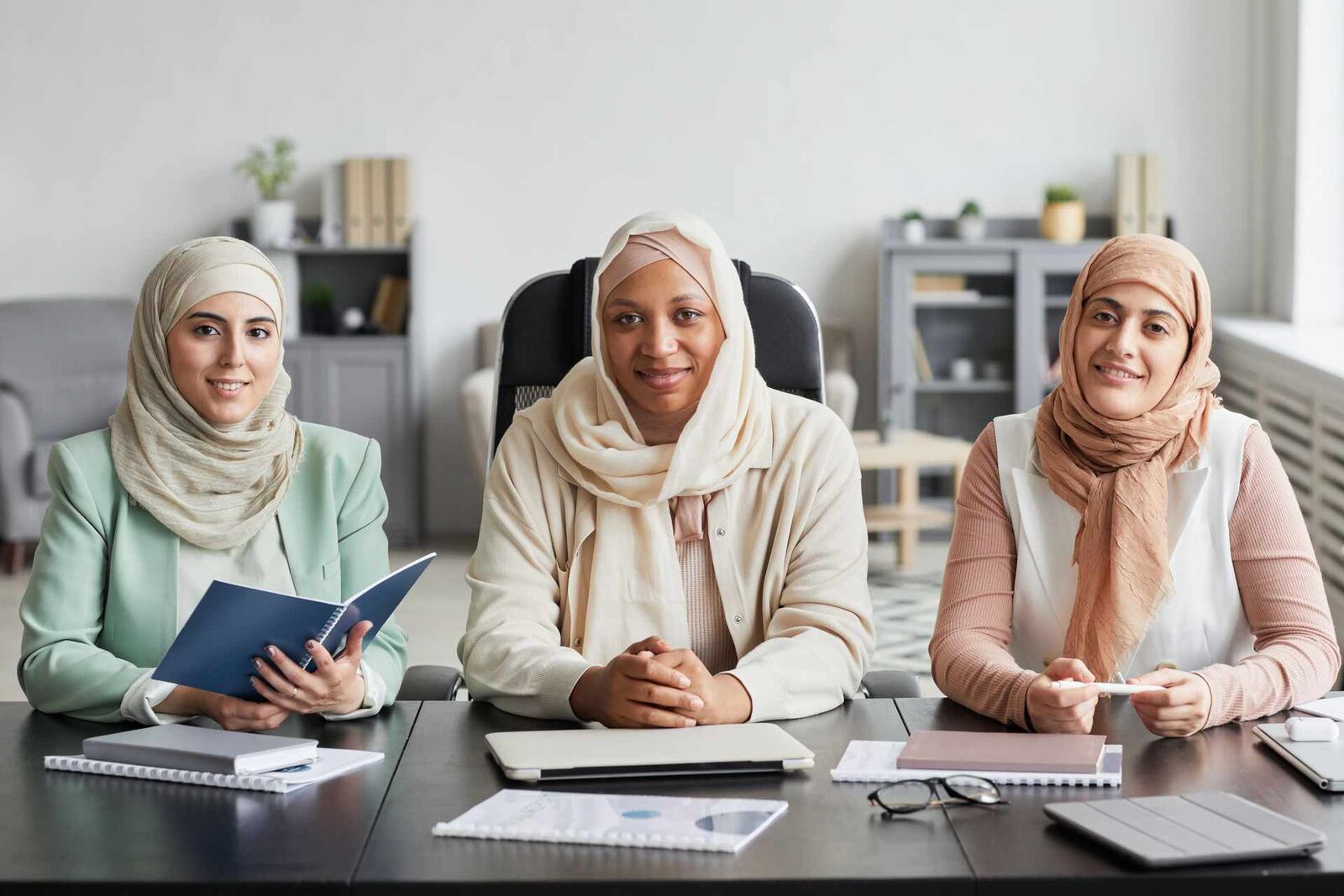Three colleagues in business attire sit together at a conference table reviewing documents in a bright office