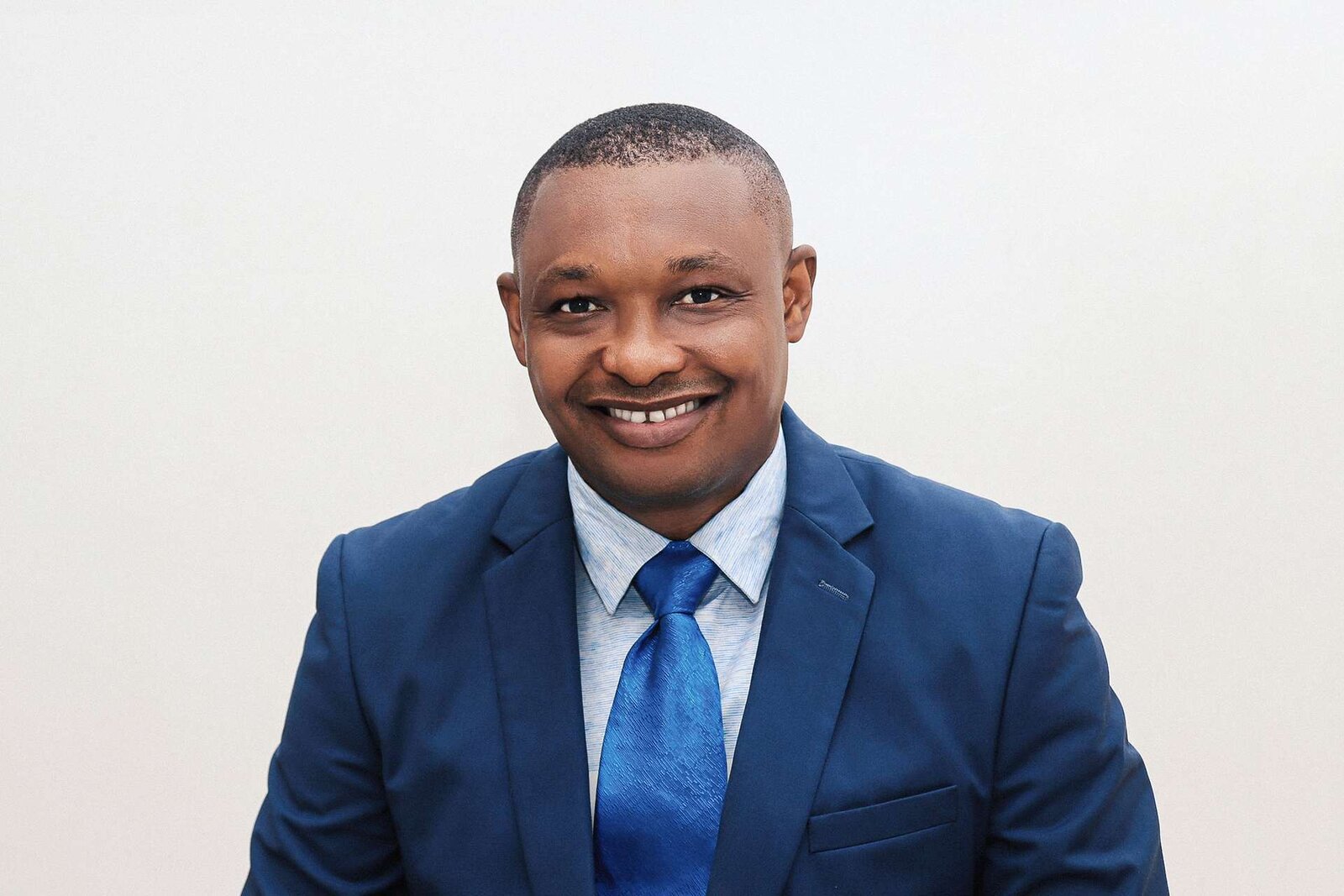 A smiling professional in a blue suit poses for a studio portrait