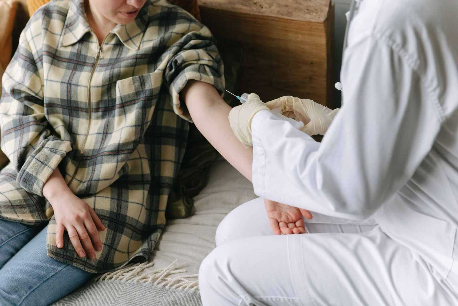 A clinician in a white coat administers an injection into a seated patient's upper arm during a home visit, a generic stand-in for vaccine administration; not Nuravax's own clinical site