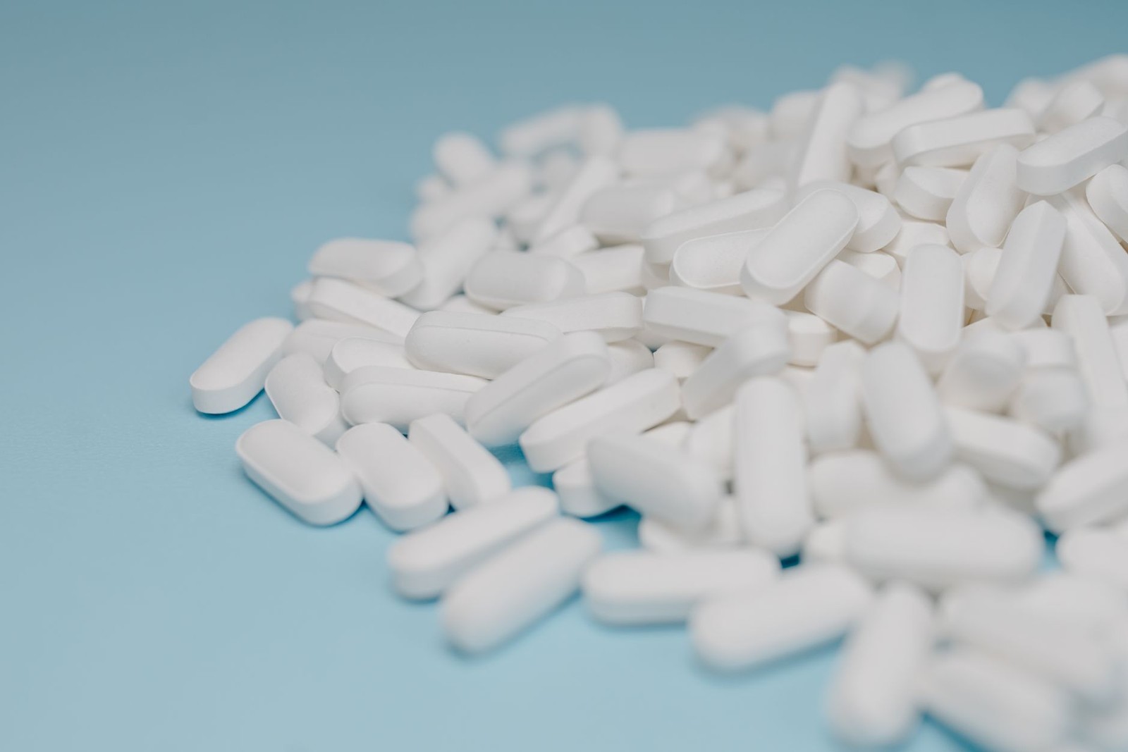 A loose pile of white, oblong pharmaceutical tablets spread across a light blue background