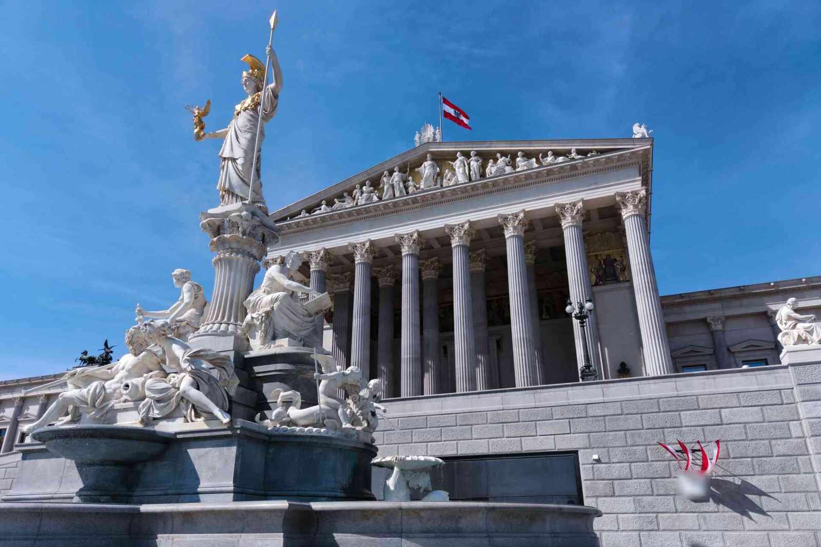 The Austrian Parliament building in Vienna behind the Athena fountain under a clear blue sky, a generic European-institutional stand-in