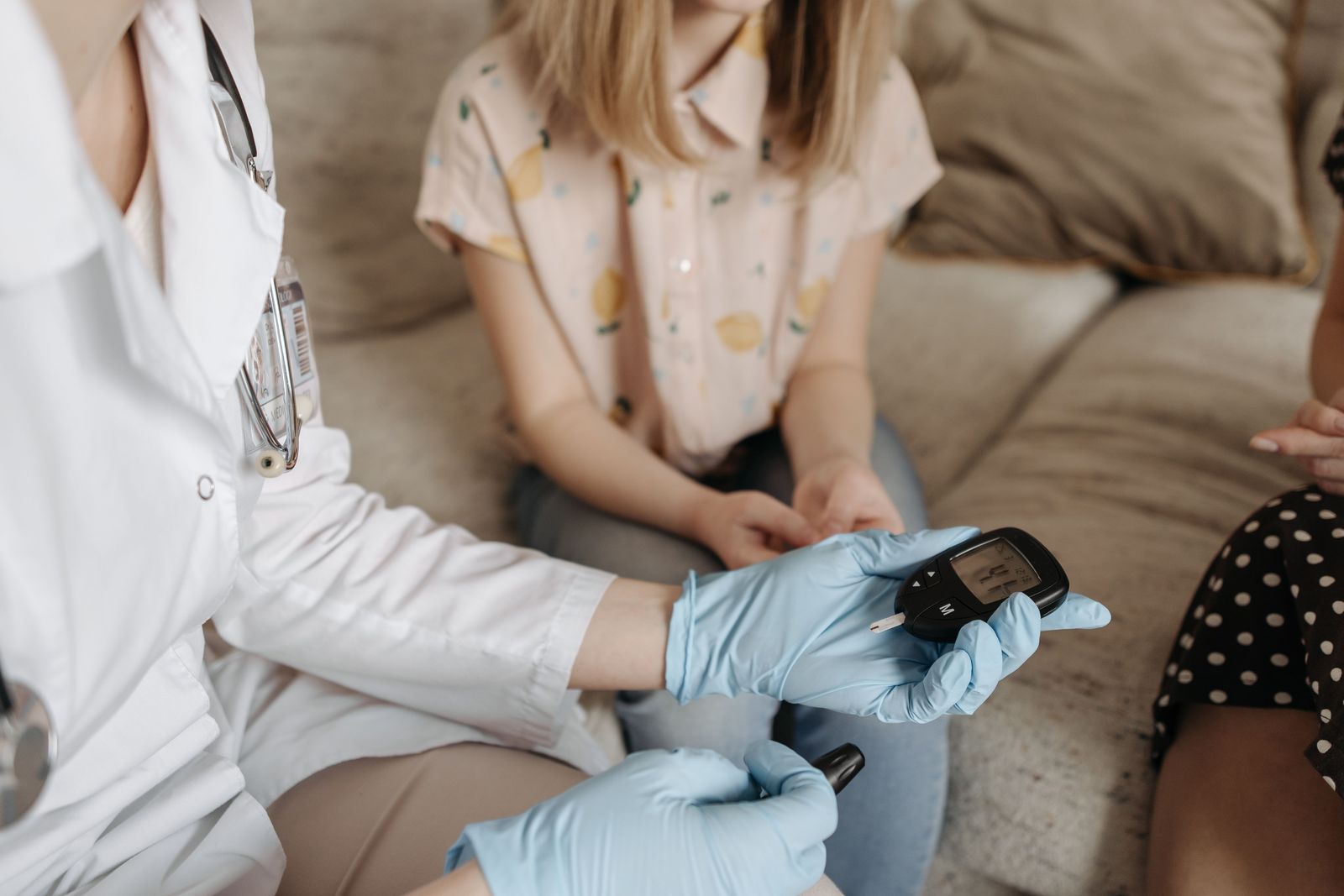 A physician in a white coat and gloves checks a patient’s blood glucose with a meter during a consultation