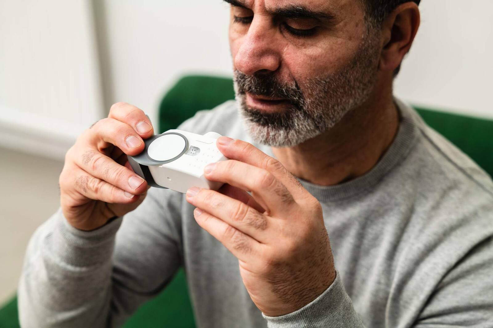 A man closely examines a small white electronic medical device held in both hands