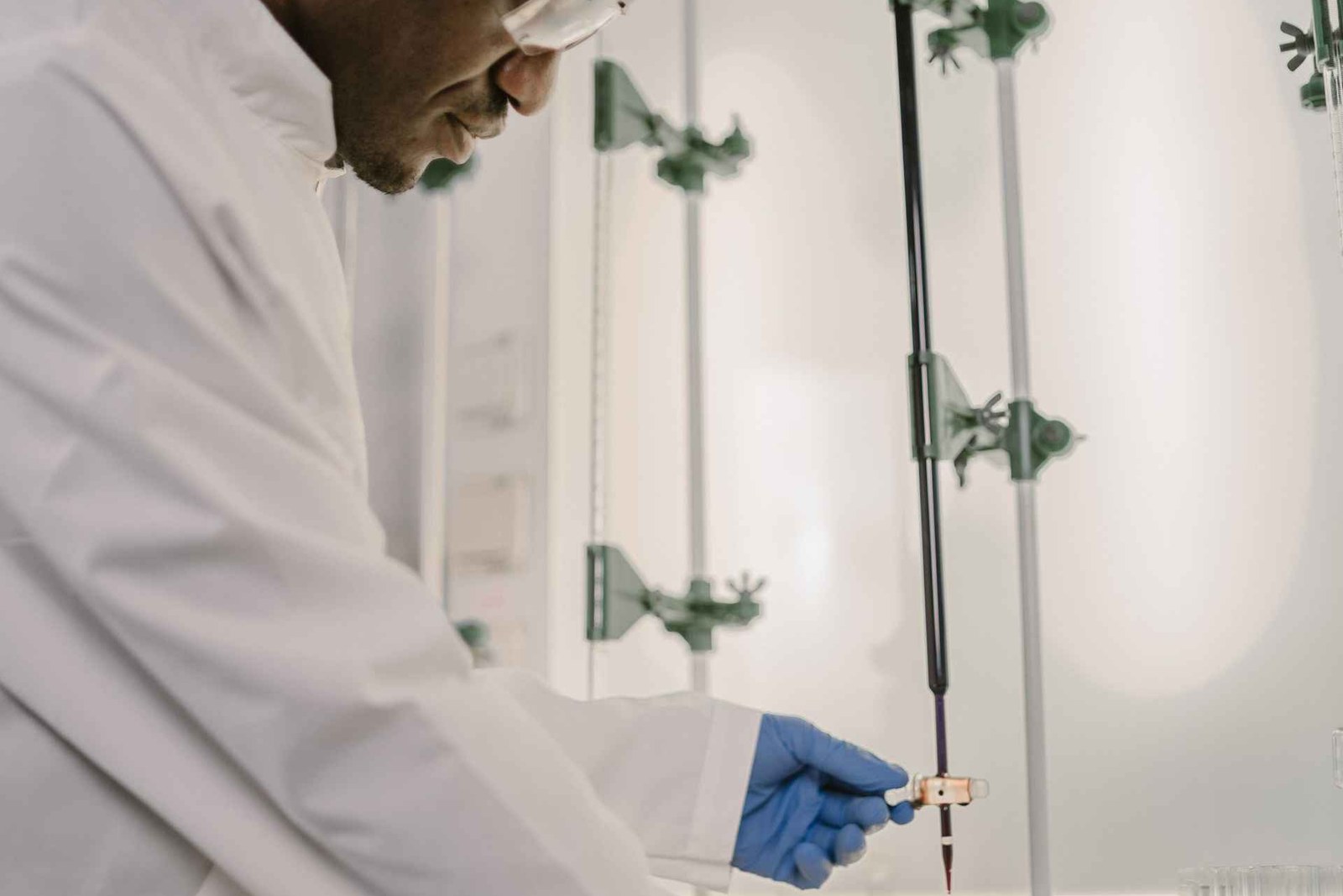 A researcher in a white lab coat and blue nitrile gloves handles laboratory titration equipment while wearing safety glasses