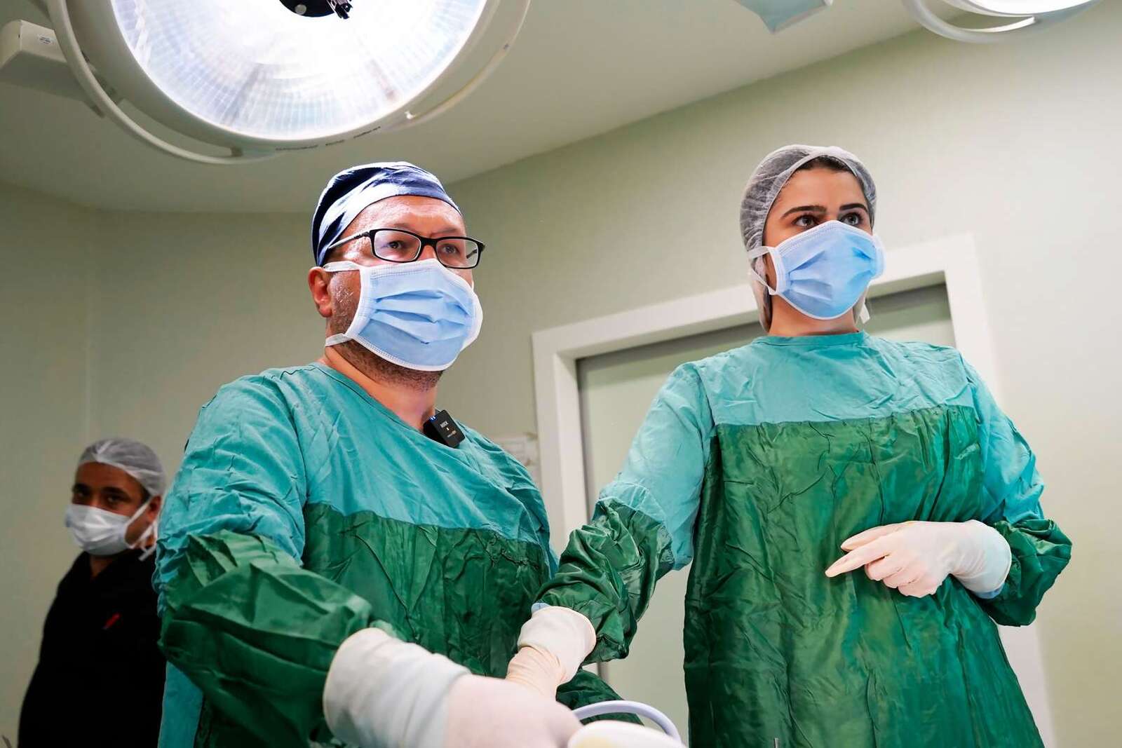 Two surgeons in green gowns and masks in a bright operating room, a generic stand-in for a transcatheter valve-repair procedure