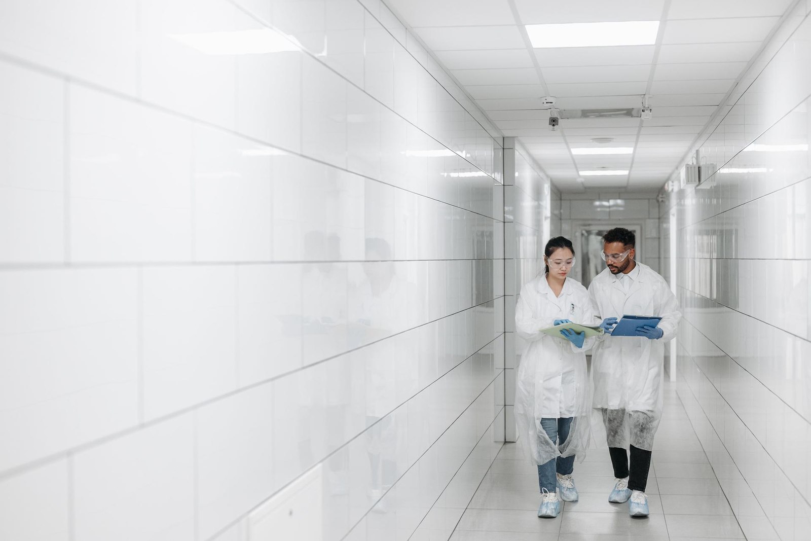 Two gowned staff walking and reviewing notes together in a bright cleanroom corridor