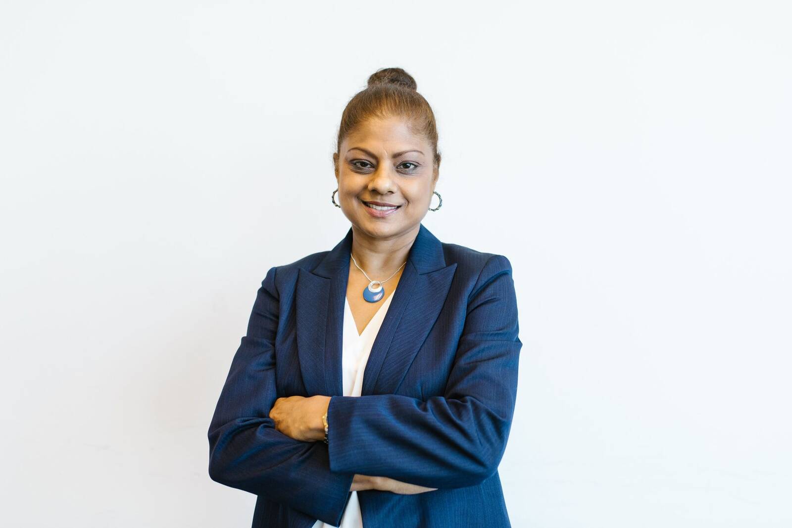A woman in a dark blazer standing with arms crossed against a plain white wall
