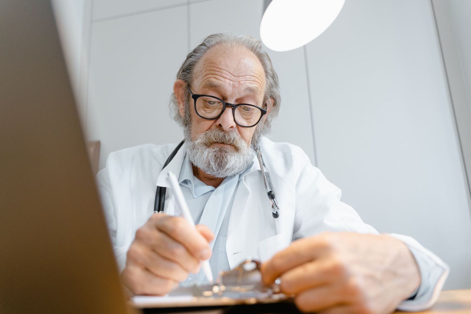 A physician in a white coat reviews a patient's chart on a clipboard
