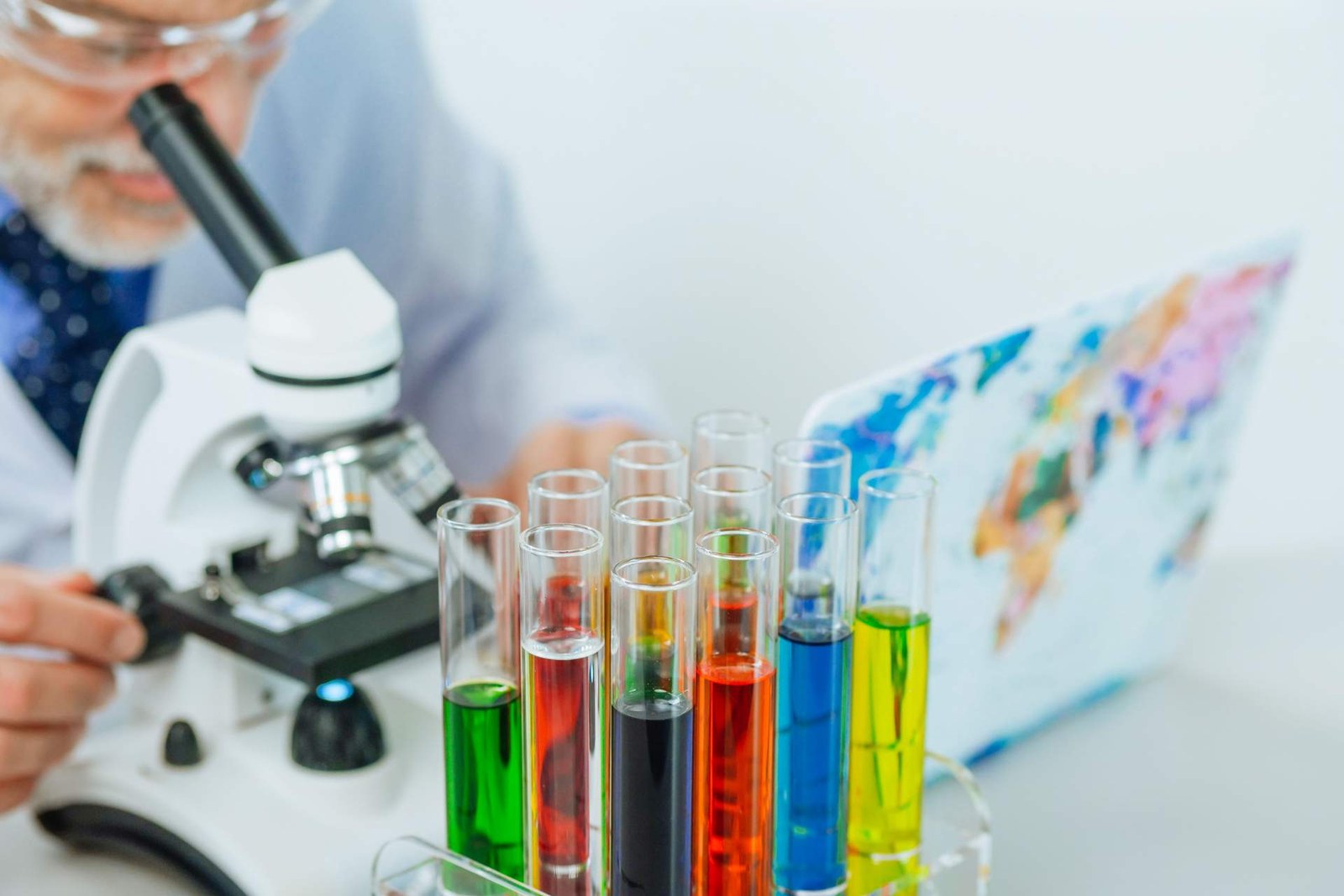 A scientist examines colorful test tubes and vials under a microscope in a laboratory