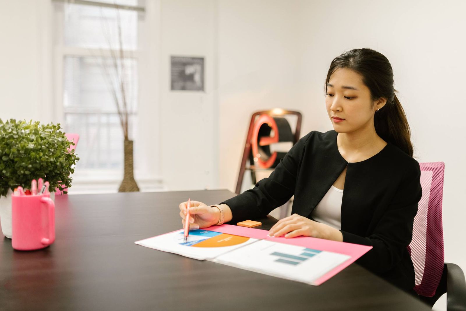A professional in a dark blazer reviews a colorful bar and pie chart report at a desk in a bright office