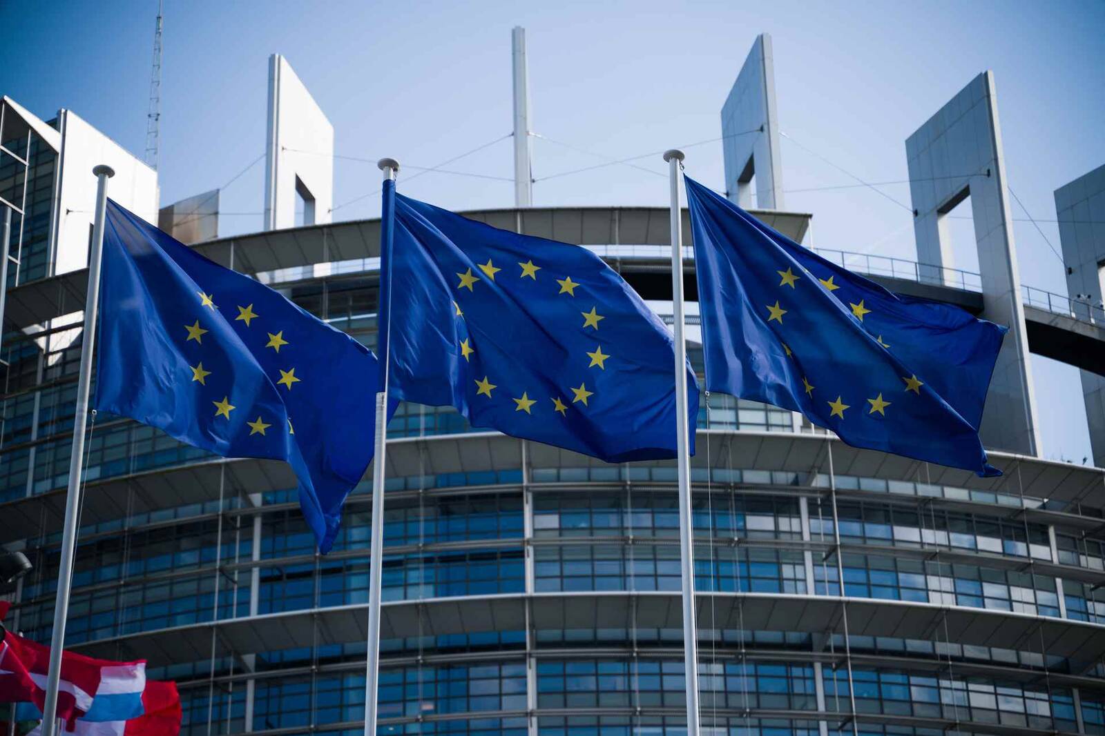 European Union flags flying in front of the European Parliament building in Strasbourg under a clear sky