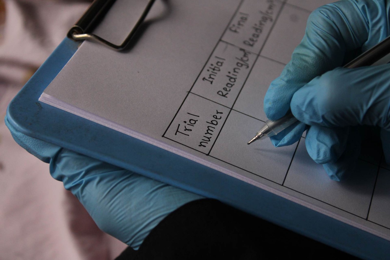 A gloved hand records readings on a clinical trial data sheet on a clipboard