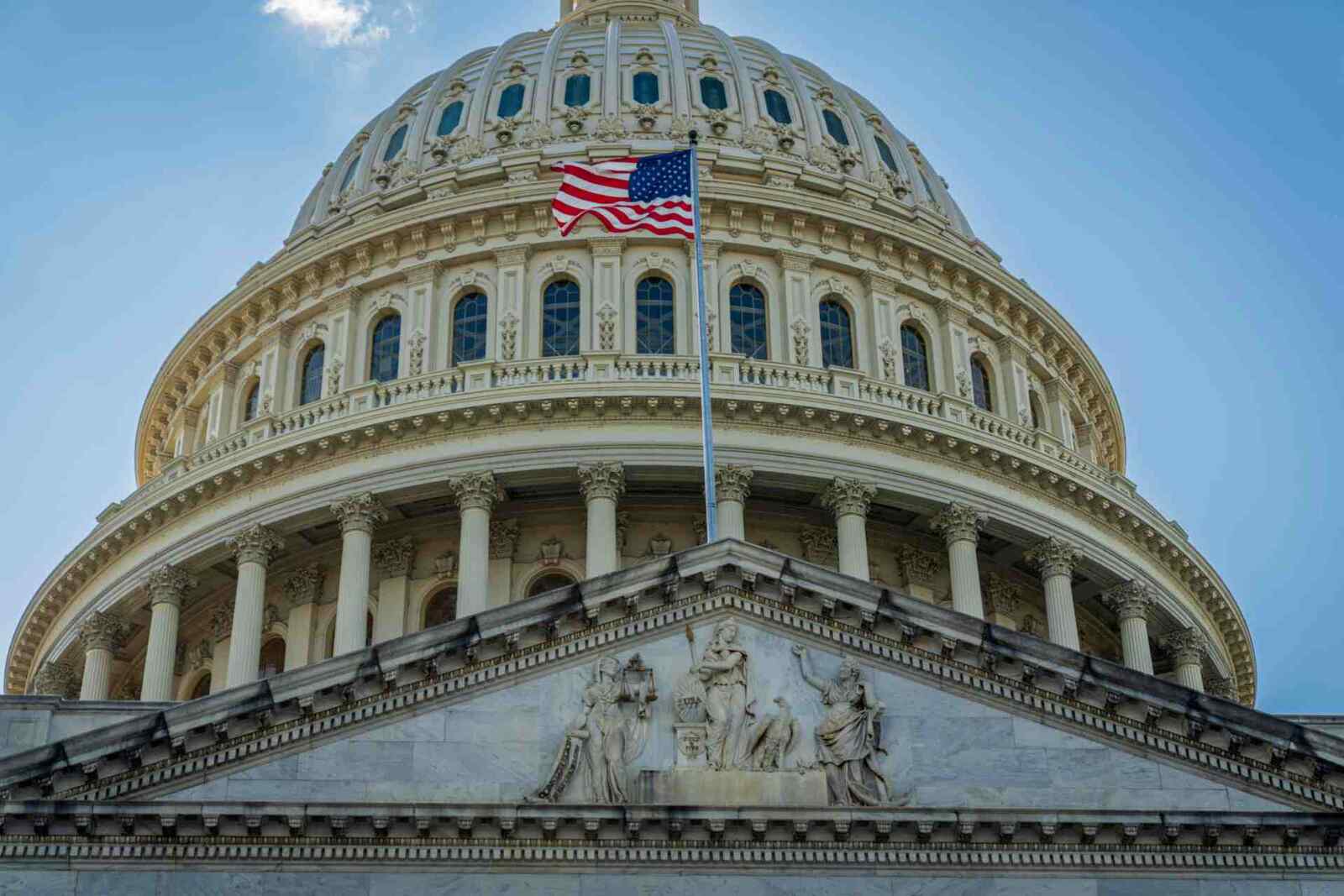 A close-up of the U.S. Capitol dome with an American flag flying against a blue sky