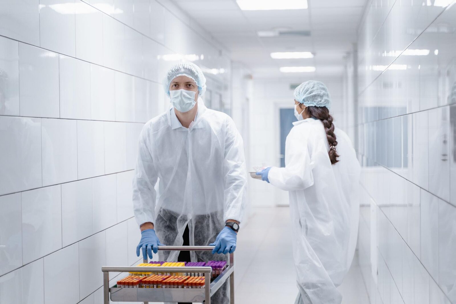 Lab staff push a sample cart through a bright cleanroom corridor
