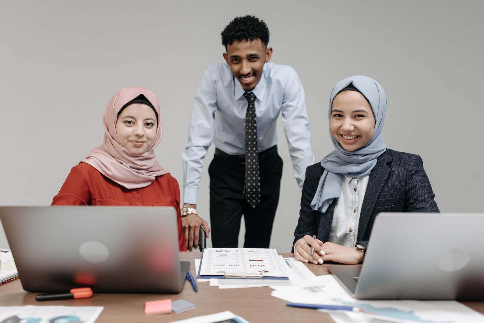 Three colleagues at laptops reviewing a printed chart-filled report together in a bright office