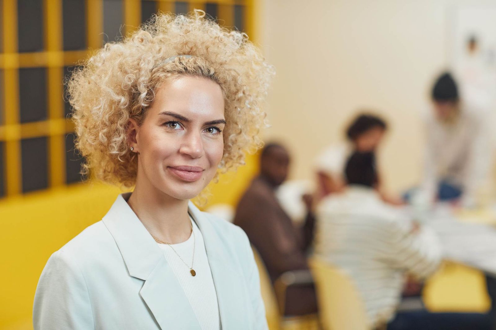 A businessperson in a blazer stands for a team portrait in a modern office setting