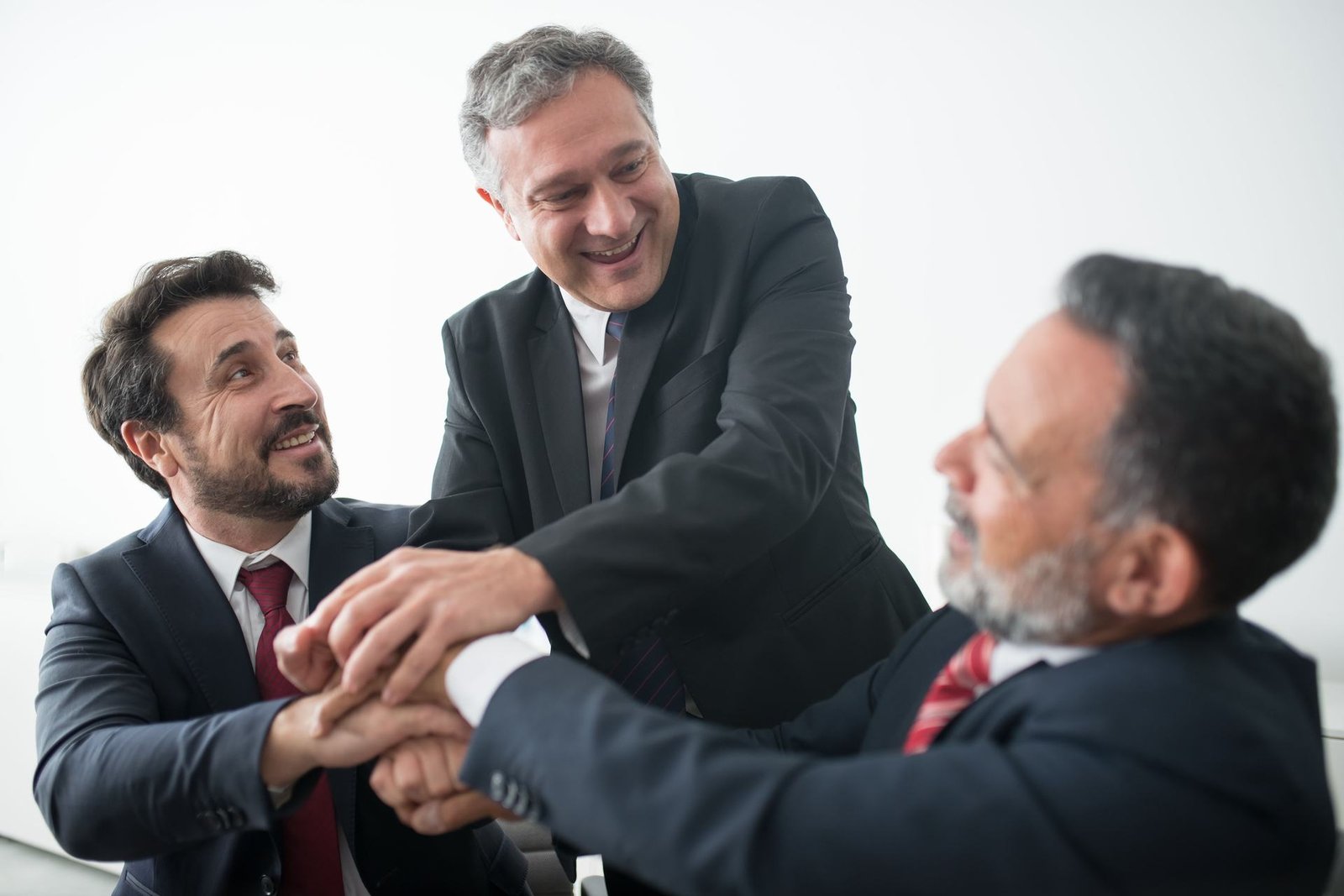 Three executives in business suits clasp hands together in a celebratory gesture