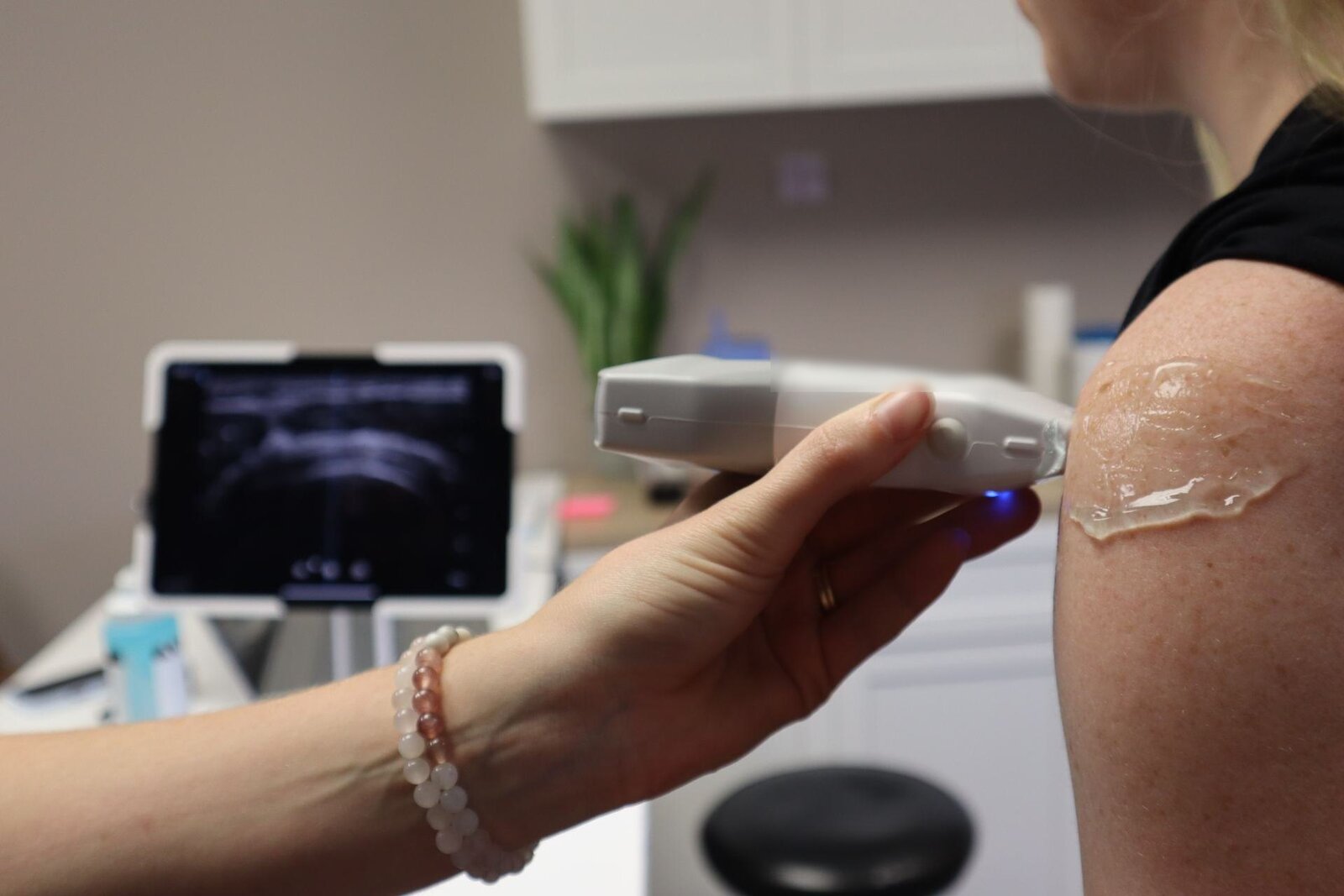 A clinician uses a handheld ultrasound probe to examine a patient's shoulder joint in a clinic, a generic stand-in for rheumatologic assessment