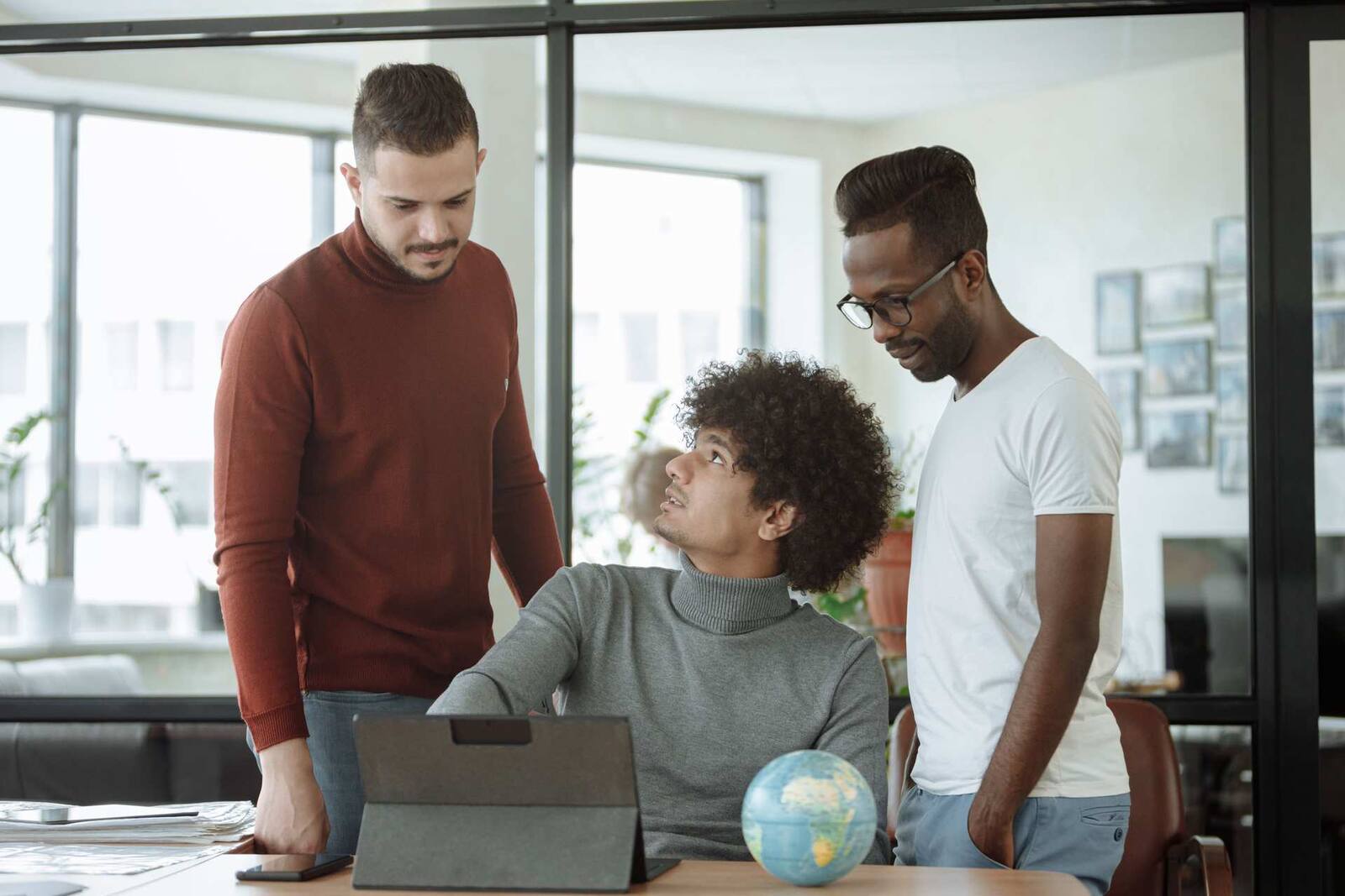 Three colleagues reviewing a tablet around an office desk, a generic stand-in for a pharmaceutical company's commercial or medical-affairs team — not Pfizer's own staff