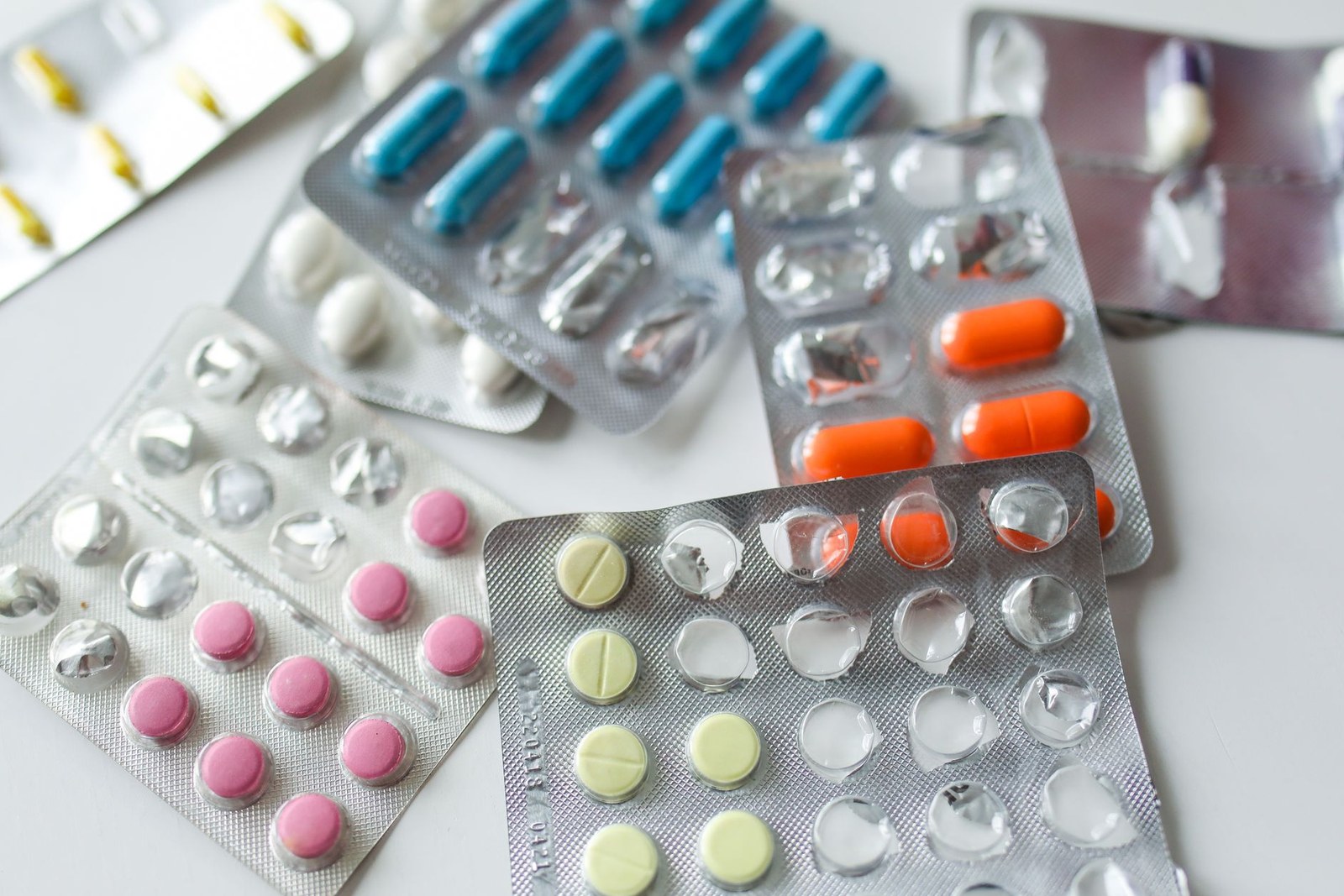 An assortment of pharmaceutical blister packs holding pills and capsules of varying colors spread across a white surface