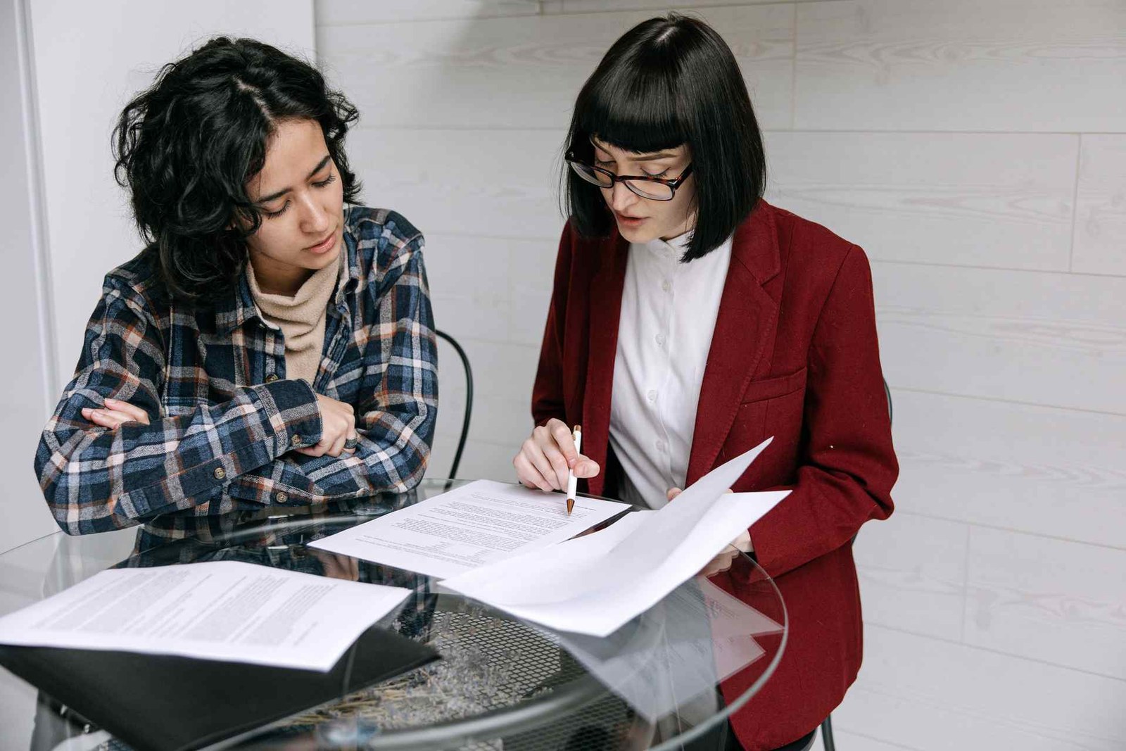 Two colleagues review a signed legal document together at a glass table, one holding a pen to the page