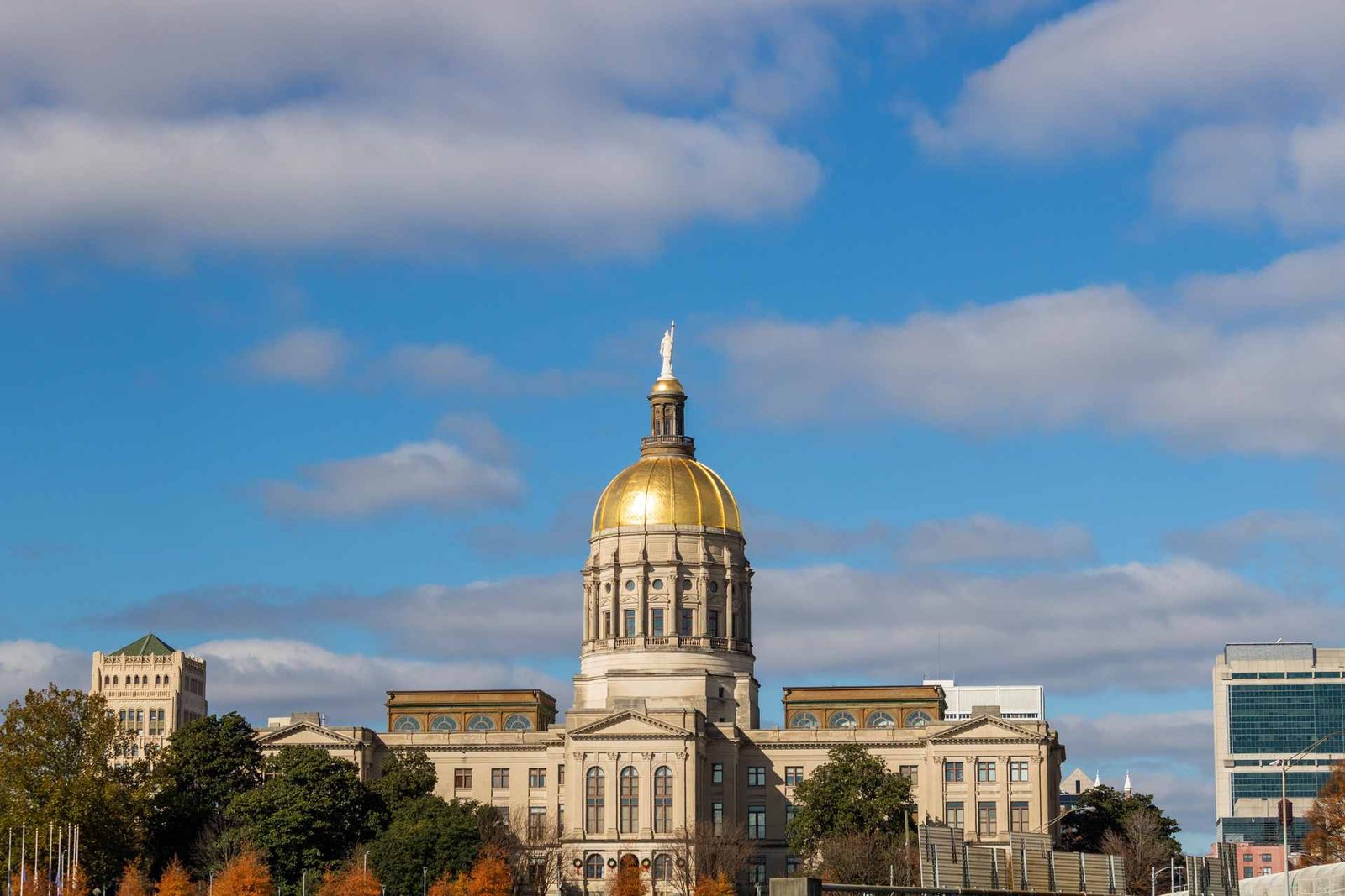 The gold dome of the Georgia State Capitol building rises against a partly cloudy blue sky