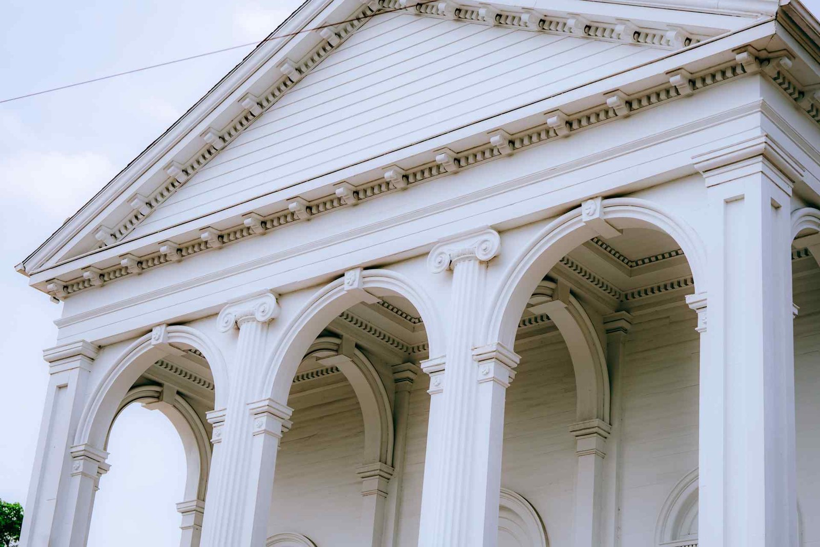 A close-up of a white neoclassical building's pediment and arched colonnade against a pale sky