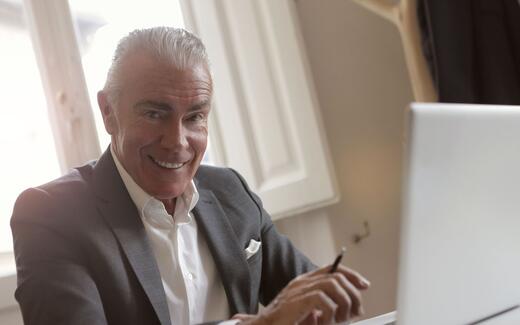 A business professional smiles while working at a laptop in a sunlit office