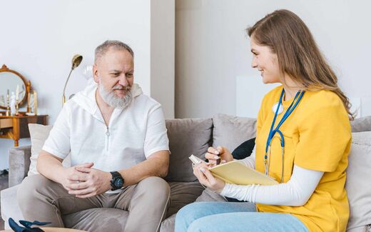 A clinician reviews notes with an older patient during a home consultation