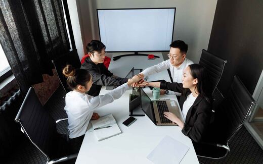 A team stacks hands together over a conference table in a gesture of shared success