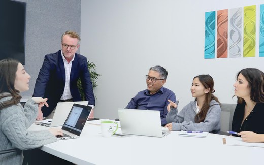 Three senior executives review printed charts and a laptop together at a conference table