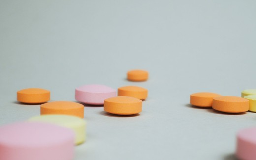 Loose orange, pink, and yellow tablets scattered across a light gray surface, softly out of focus