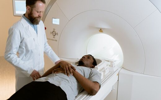 A physician in a white coat positions a patient at the entrance of an MRI scanner