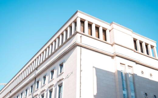 A white institutional office building photographed from below against a clear blue sky