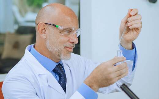 A senior scientist in a tie uses a pipette with a test tube in a bright laboratory