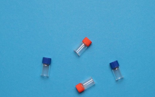 Four small glass vials with red and blue caps scattered across a blue background