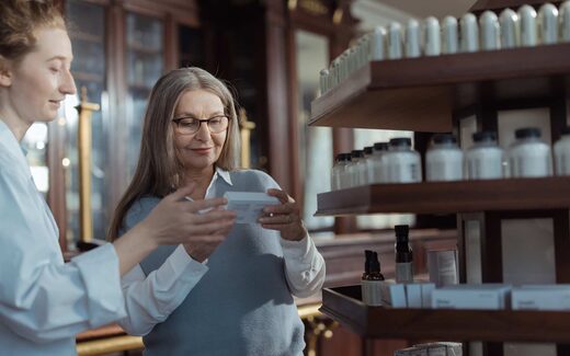 A pharmacist and a customer examine a medication package in a pharmacy