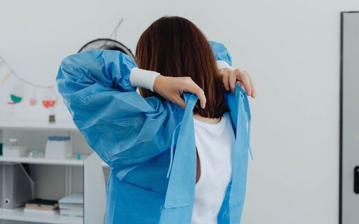 A clinician ties a blue surgical gown in a clinical setting, a generic pre-procedure stand-in