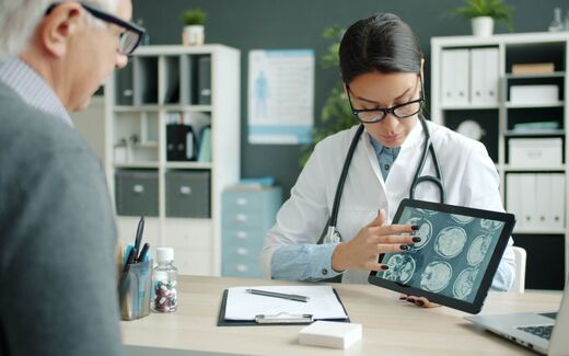 A physician shows a seated patient brain-scan images on a tablet computer