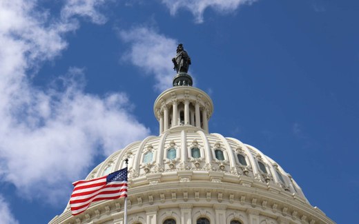 The dome of the U.S. Capitol building with an American flag flying in front against a blue sky