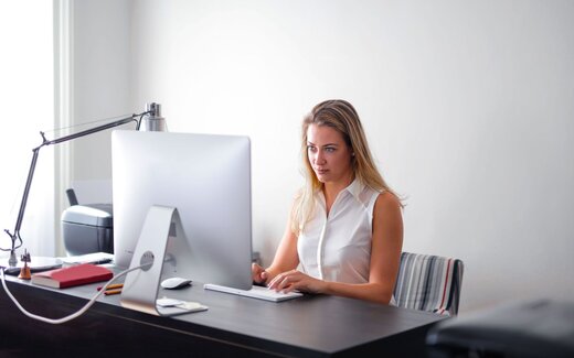 A clinician in a white blouse reviews data on a monitor in a bright white office