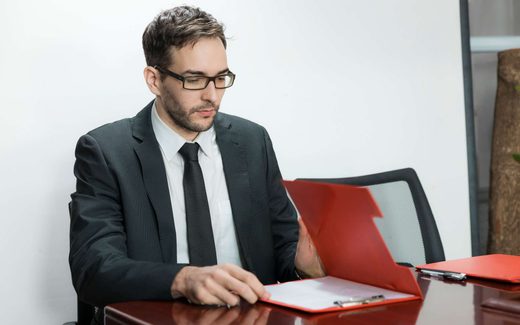 A businessman in a suit reviews a red folder open on a boardroom table