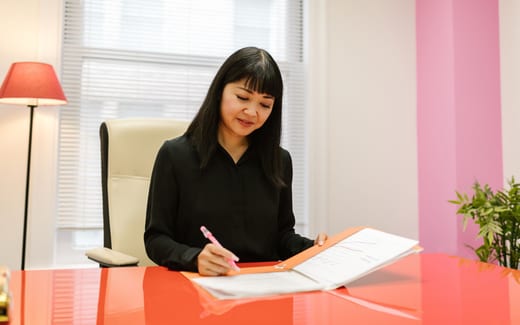 A professional reviews paperwork from an orange folder at a desk