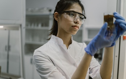A researcher in safety glasses and blue gloves inspects a laboratory sample