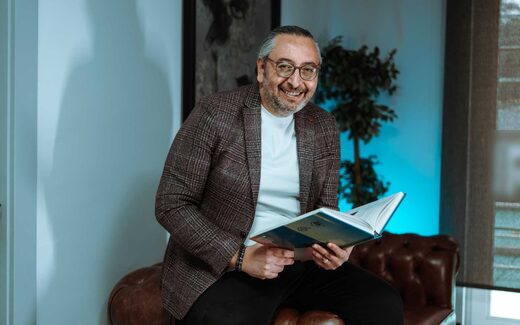A smiling executive in a plaid blazer reviews a bound document in an office lounge